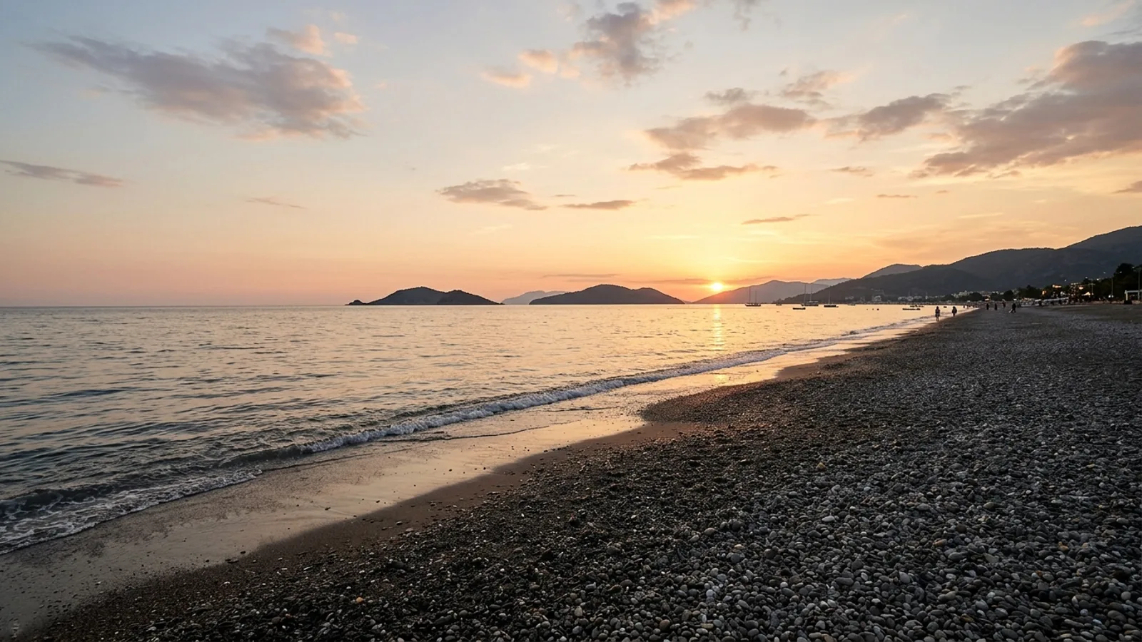 Calis Beach, Türkiye — the long straight pebble beach at Calis near Fethiye, a flat shore facing west across the bay towards low islands at sunset.