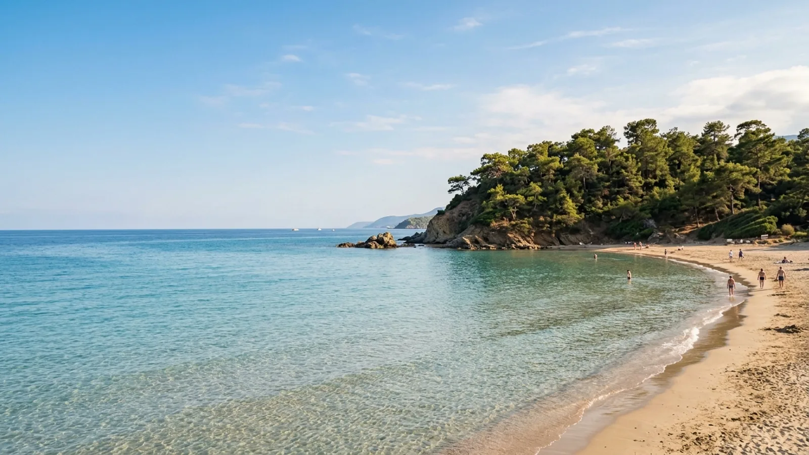 Incekum, Türkiye — the shore at Incekum west of Alanya, a small sandy cove with very shallow clear water and a pine-covered headland to one side.