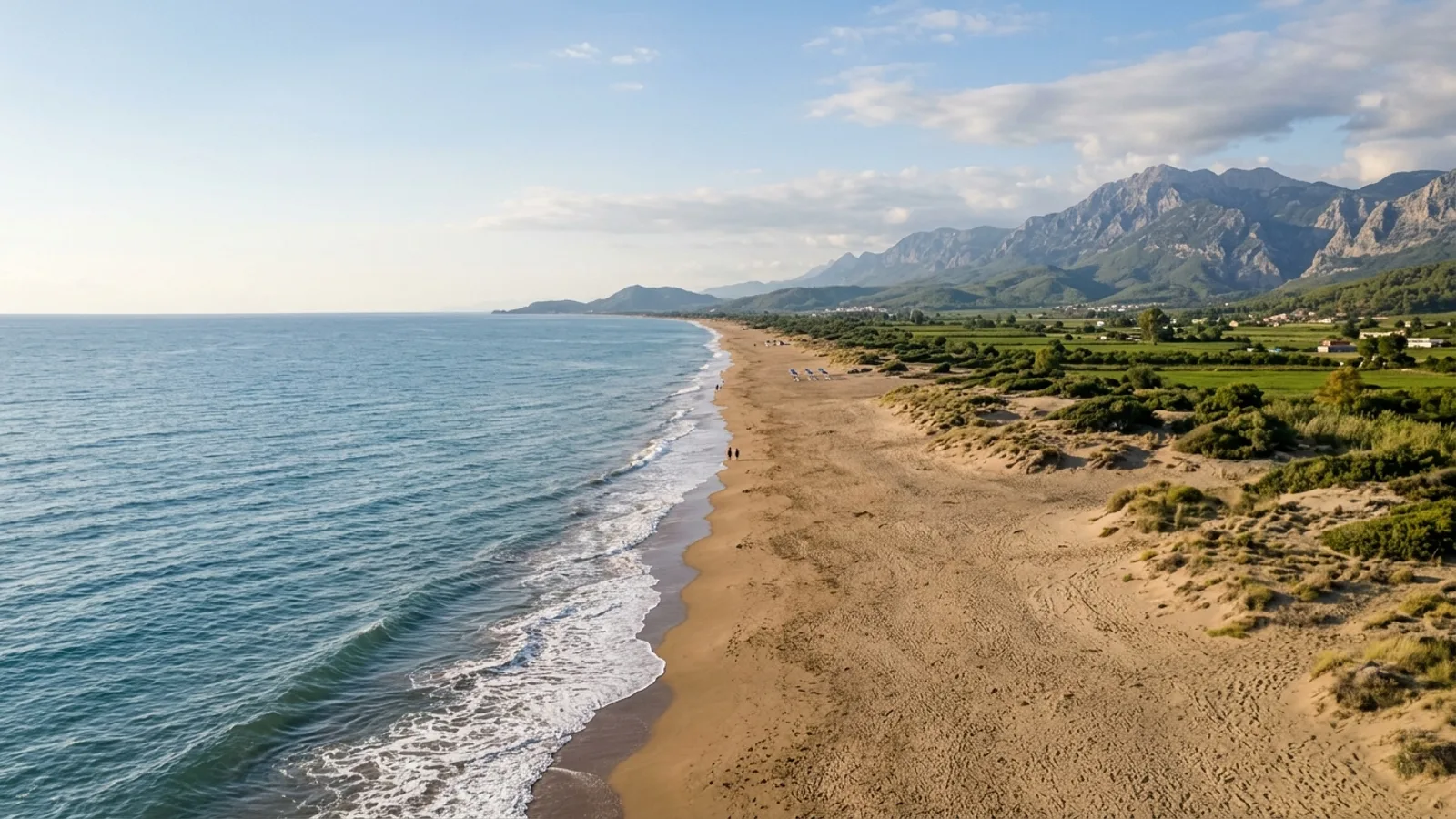 Kizilot, Türkiye — the long open sandy beach at Kizilot on the Antalya coast, low dunes and a flat green hinterland with distant mountains.