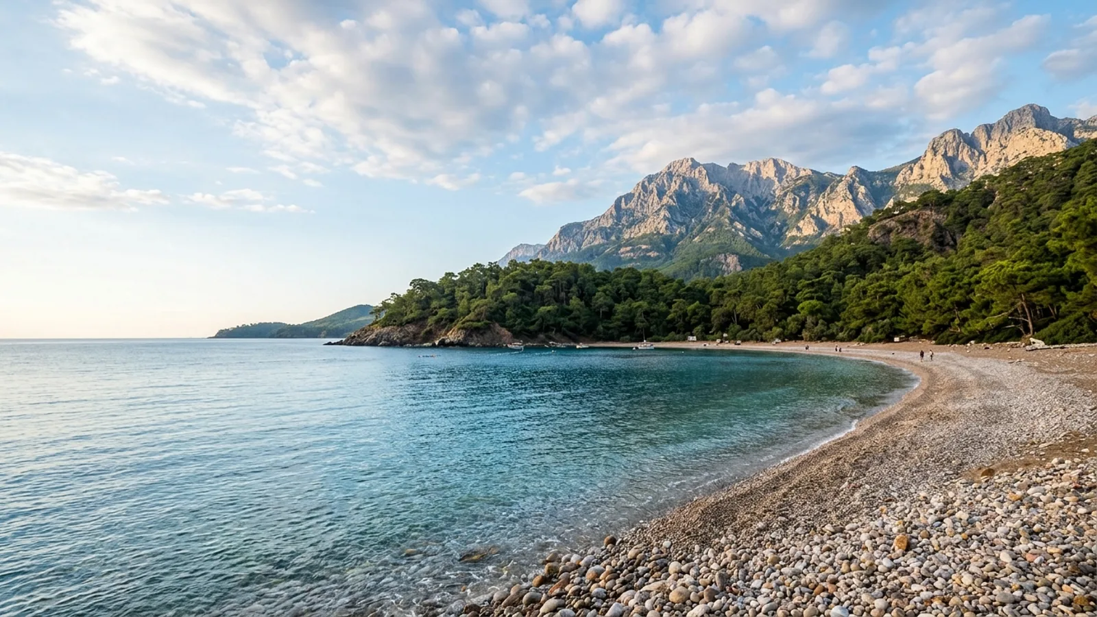 Tekirova, Türkiye — the coast at Tekirova, a sheltered pebble bay ringed by dense pine forest with the high Taurus ridge behind.